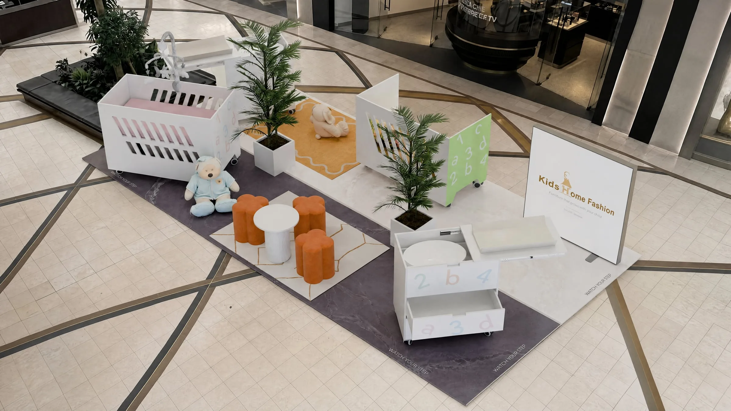 Childrenswear kiosk with white display units, planting and soft seating