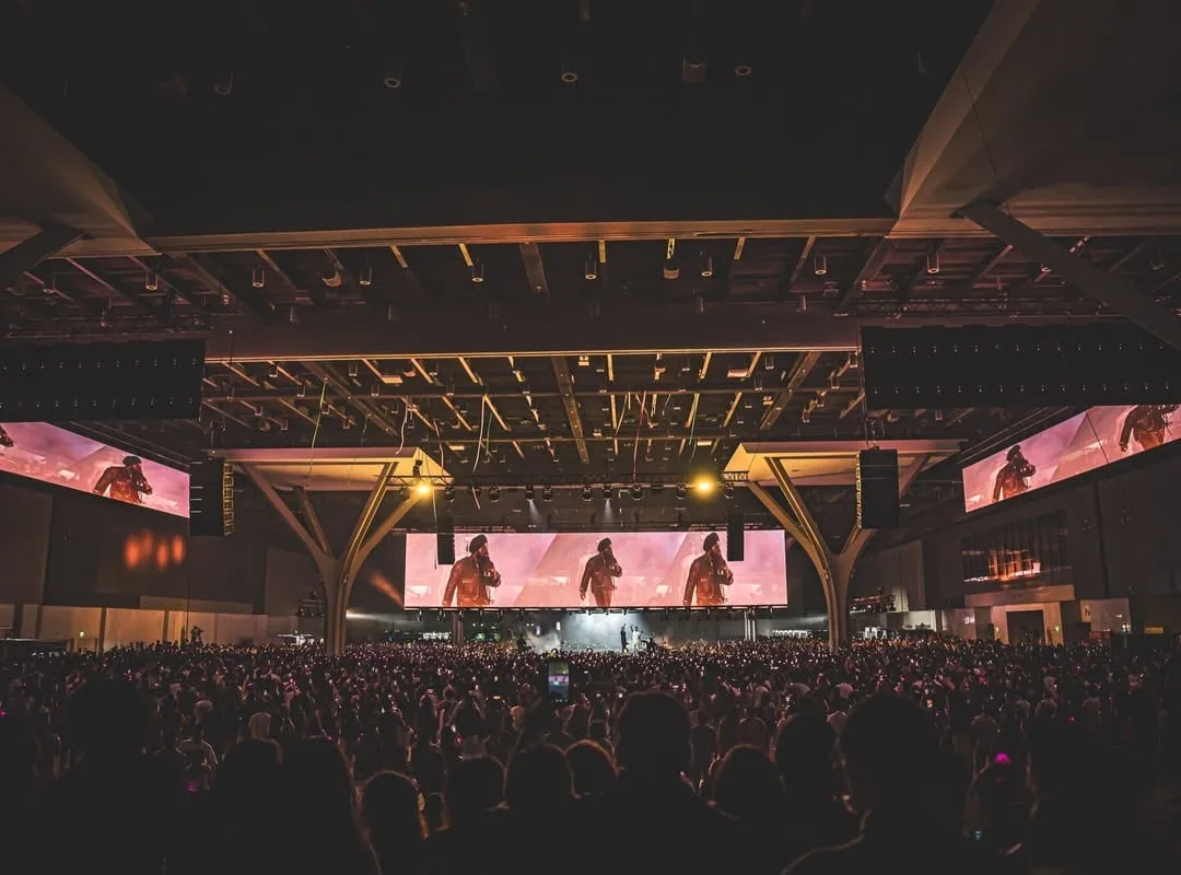 View from the back of a covered amphitheatre, screens flanking the stage across a full house
