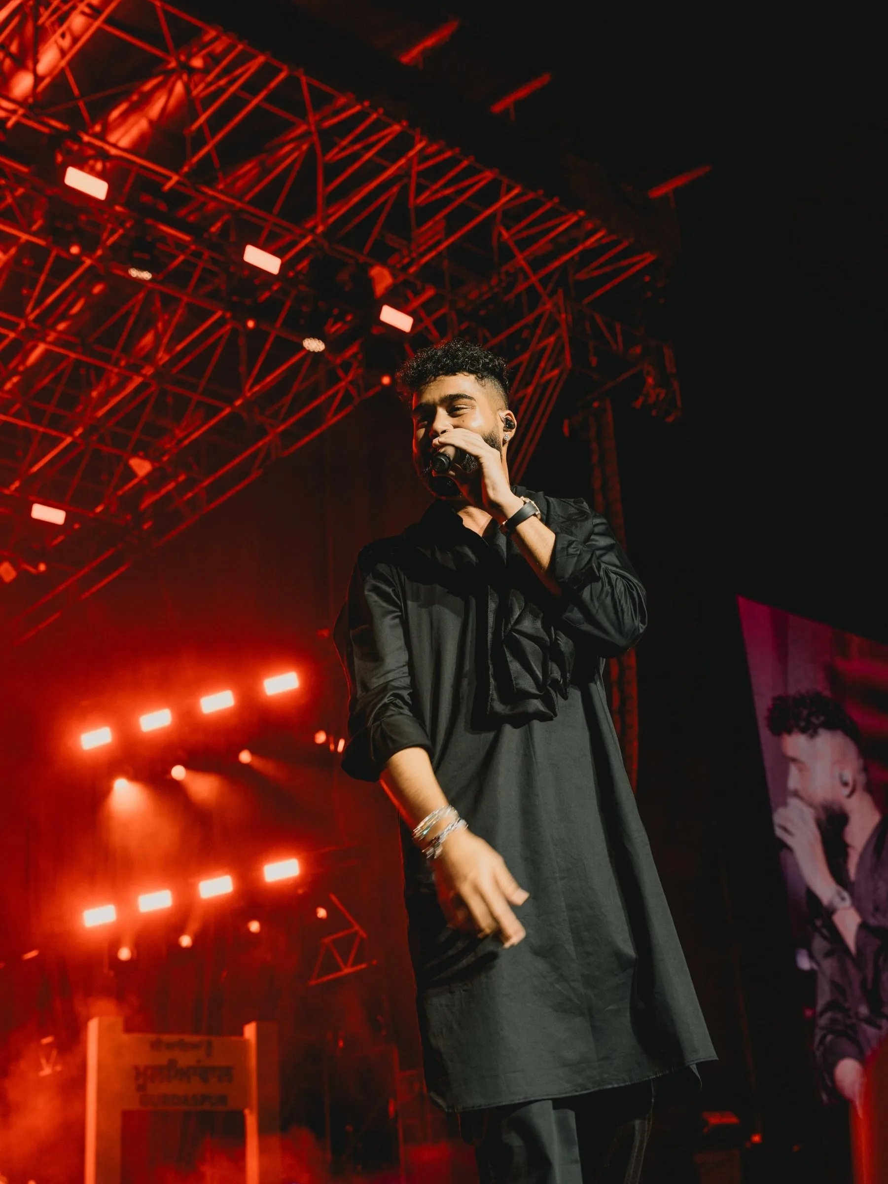 The artist performing in red stage light with the screen behind