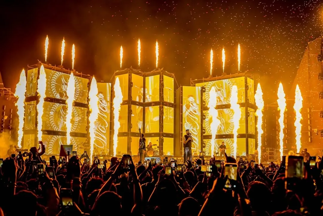Gold screens with circular motifs, pyro columns and confetti over a raised crowd